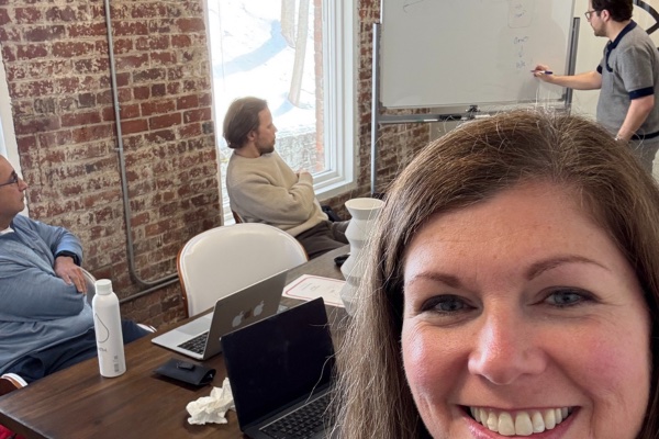 A smiling selfie from an early Tonotop planning session: teammates around a wooden table in a brick-walled room while one sketches on a whiteboard.
